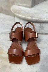 Sandalias de cuero color champagne, con punta cuadrada, tira ancha sobre el empeine y tira al tobillo con hebilla metálica. Taco cuadrado de 7 cm.