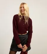 Cardigan cropped color borgoña de punto, con cuello redondo, manga larga, cierre frontal con botones y bolsillos delanteros.