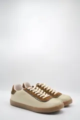 Zapatillas bajas color beige con detalles en marrón y cordones blancos.