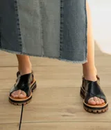 Sandalia de cuero vacuno color negro, con suela de goma deportiva, hebilla al tobillo y horma ancha.