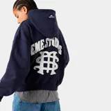Hoodie azul marino con capucha y cordón ajustable, corte oversize y puños y cintura acanalados. Estampado frontal y trasero con el nombre de la marca y un símbolo gráfico.