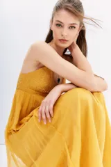 Vestido largo color mostaza, con breteles finos cruzados en la espalda y detalles de canutillos bordados.