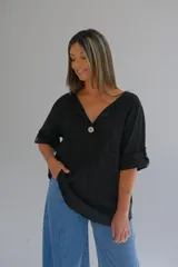 Blusa negra de algodón con diseño de puntos en relieve, corte acampanado, escote en V, mangas 3/4 con botón para ajustar el largo y un botón de nácar en el escote.