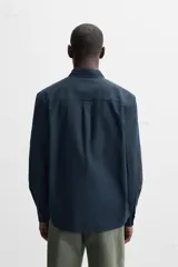 Camisa azul marino de corte regular fit, confeccionada en tejido de algodón Oxford. Tiene cuello abotonado, manga larga con puños abotonados, bolsillo de parche en el pecho y cierre frontal con botones.