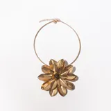 Collar dorado con dije grande en forma de flor con pétalos facetados y centro con cuentas negras. El collar es rígido y tiene una cadena extensible con cierre de mosquetón.
