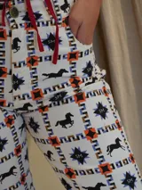 Pantalón de jean blanco con estampado de caballos negros, estrellas azules y motivos geométricos en naranja. Corte recto con aberturas en el ruedo.