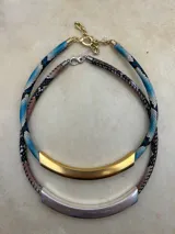 Gargantilla corta con cordón tubular estampado símil piel de serpiente y dije tubular metálico. Cierre con mosquetón y cadena de alargue.