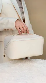 Neceser color beige de símil cuero con cierre sesgado, asa y compartimentos internos.