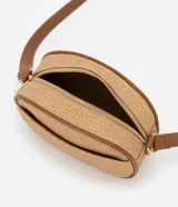 Cartera bandolera pequeña color beige con textura de paja y detalles en marrón. Tiene cierre de cremallera, bolsillo externo y asa larga regulable con hebilla.