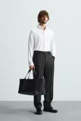Camisa color beige de corte slim fit, confeccionada en tejido elástico que minimiza las arrugas. Tiene cuello italiano abierto, manga larga con puños abotonados y cierre frontal con botones.