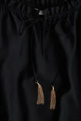 Vestido largo negro con escote cuadrado, cordón ajustable con borlas de cadena, mangas cortas abullonadas con forro y ribete elástico oculto, y costura fruncida bajo la cadera.
