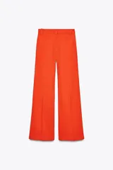Pantalón de tiro alto color naranja, corte wide leg y largo hasta el tobillo. Tiene bolsillos de parche delanteros y cierre frontal con cremallera y botón.