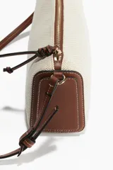 Bandolera rectangular de tela color beige con textura tipo canasta y detalles en cuero marrón. Tiene cierre superior con cremallera, correa larga regulable con hebilla y forro interior.