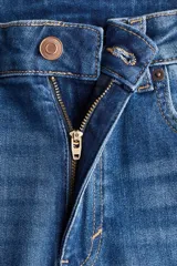 Jeans de denim azul oscuro con efecto lavado y desgaste sutil en la parte delantera de los muslos y las rodillas. Diseño de tiro alto, cinco bolsillos y corte acampanado desde la rodilla hacia el bajo.