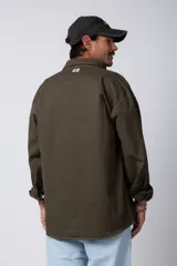 Camisa verde militar de manga larga, corte oversize, con cuello clásico, cierre frontal con botones y bolsillo en el pecho. Confeccionada en algodón suave y con costuras a la vista.