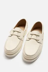 Zapato náutico color crema de cuero, con cordones alrededor del tobillo y suela plana.