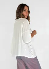 Remera color amarillo con cuello redondo y mangas cortas amplias, con detalle de botones en los laterales.