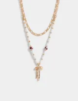Collar corto multicadena dorada, con una cadena de eslabones y otra de perlas sintéticas con cuentas florales y dije de moño metálico.