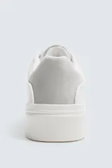 Zapatillas deportivas blancas con detalle de color marrón en el talón y suela con volumen.