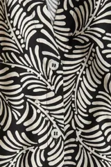 Blusa de popelina de algodón con estampado de hojas en blanco y negro. Tiene cuello mao, abertura en V con botones y mangas globo tres cuartos con puños finos.