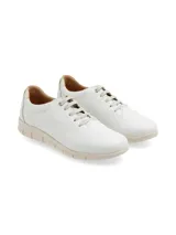 Sneaker de cuero blanco con talón dorado, cordones finos y suela beige con diseño anatómico.