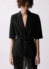 Blazer negro de lino y viscosa, con cuello de solapa, manga francesa, cinturón con hebilla y cierre frontal con botones. Tiene dos bolsillos laterales con solapa.