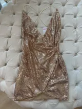Vestido corto dorado de lentejuelas con escote en V profundo, tirantes finos cruzados en la espalda y cierre invisible.