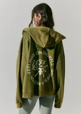 Buzo verde militar de algodón rústico con capucha, corte oversize, cierre metálico, bolsillos delanteros, estampa en frente y espalda, cordón con puntera de goma y lavado acid wash suave.