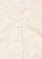 Cárdigan color crema de tejido de punto fino, corte recto, cuello redondo, manga larga, cierre frontal con botones y terminaciones en canalé.