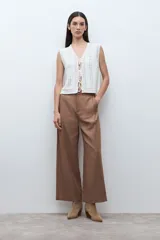 Chaleco sin mangas color blanco crudo, tejido a crochet o punto abierto, con escote en V y cierre frontal mediante lazos cruzados.