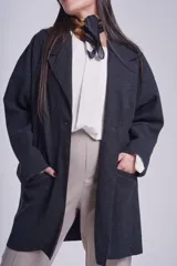 Tapado gris oscuro de corte oversize, con solapa clásica, hombros caídos, cierre con un botón central y bolsillos laterales funcionales.