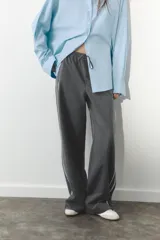 Pantalón de tiro alto negro a rayas verticales blancas, con cintura elástica ajustable con cordones, bolsillos delanteros y banda lateral blanca.