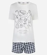 Conjunto de pijama de dos piezas compuesto por una remera de manga corta color blanco tiza con estampa de frutas en negro y un short estampado a cuadros en tonos azules y blancos.