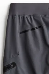 Pantalón de jogging deportivo gris oscuro, de corte ajustado, con cintura elástica ajustable con cordón, bolsillos laterales y bolsillos con cierre en las piernas.
