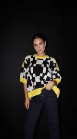 Sweater de punto con mangas cortas, estampado geométrico en blanco y negro, y ribetes amarillos en cuello, puños y ruedo.