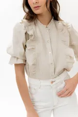 Blusa de lino color rojo con volados frontales que enmarcan el pecho, cuello redondo con mini volado y mangas 3/4 abullonadas con puño elástico. Presenta un cierre frontal con botones y una silueta relajada.