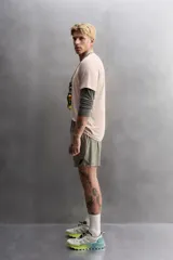 Shorts de entrenamiento color verde oliva, confeccionado en tejido técnico ligero y elástico con perforaciones. Tiene forro interior, cintura elástica ajustable con cordón, bolsillos laterales, bolsillo trasero con cierre de cremallera, bajo con aberturas laterales y logo estampado en la pierna.