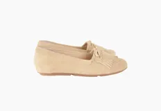 Mocasín color beige de cuero gamuzado con flecos y lazo con herrajes metálicos dorados en la capellada. Interior forrado en cuero y suela de goma flexible.