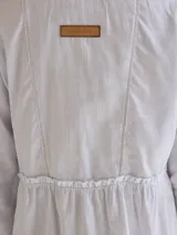 Camisa celeste de algodón con cuello clásico, cierre frontal con botones y mangas largas. Presenta volados en el frente y corte evasé.