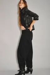 Pantalón de jean negro, tiro medio-alto, con calce holgado y piernas anchas que se estrechan hacia el tobillo. Presenta pinzas en la zona de las rodillas que acentúan su forma balloon y un recorte en el lateral. Confeccionado en denim rígido con lavado suavizado.