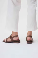 Sandalias bajas de cuero color marrón con tiras cruzadas y detalle de tira delgada color rosa.