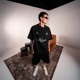 Remera negra de corte holgado con cuello redondo y mangas cortas. Presenta un estampado frontal en blanco con el texto "Nel cuore -Napoli 98-" en tipografía cursiva y dos pequeños logos gráficos.