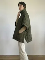 Poncho acolchado color mostaza con cuello alto y abertura frontal con cierre. Presenta un patrón capitoné de formas ovaladas y bolsillos delanteros.