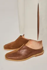 Zuecos color beige confeccionados en cuero vacuno, con punta cuadrada y suela plana color negro.