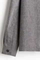 Sobrecamisa gris de tejido suave con cuello inglés, tapeta lisa, corte estándar, bolsillos superiores abiertos, abertura con botón en los puños, canesú en la espalda y bajo recto.