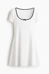 Vestido mini blanco de manga corta en punto de algodón acanalado con pollera evasé. Modelo con cuerpo entallado y escote redondo amplio con ribete fino en color negro y moña decorativa de satén. Ribete sobrehilado en mangas y bajo.