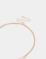 Collar corto multicadena dorada con una cadena de eslabones, una de perlas y una de eslabones con dije de flor blanca.