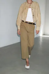 Pantalón cropped color beige de tiro alto y corte recto, confeccionado en algodón. Cuenta con bolsillos delanteros y traseros, trabillas en la cintura y cierre frontal con cremallera y botón.