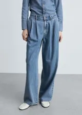 Pantalón de jean celeste de corte wide leg, tiro medio, con pinzas delanteras y cierre de cremallera y botón.