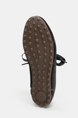 Zapato plano tipo bailarina de estilo deportivo, color negro, con pespuntes blancos contrastantes en el cuerpo y puntera. Presenta un escote redondo y un lazo decorativo en el empeine. La suela es fina y de color marrón claro.